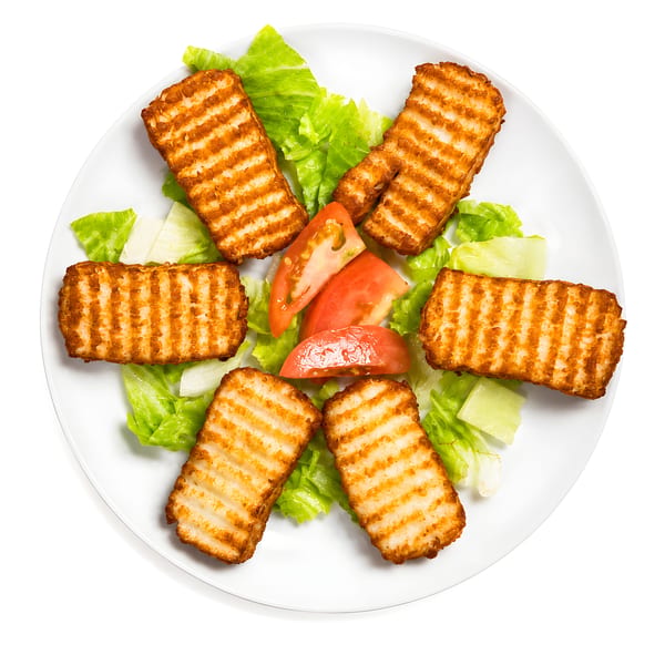 Grilled halloumi cheese slices, lettuce, and tomato wedges on a white plate.