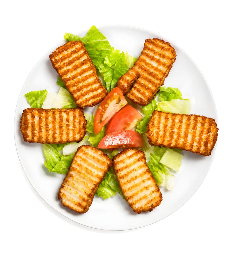 Grilled halloumi cheese slices, lettuce, and tomato wedges on a white plate.