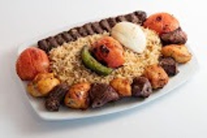 Platter of grilled kebabs, rice, and roasted tomatoes on a white background.
