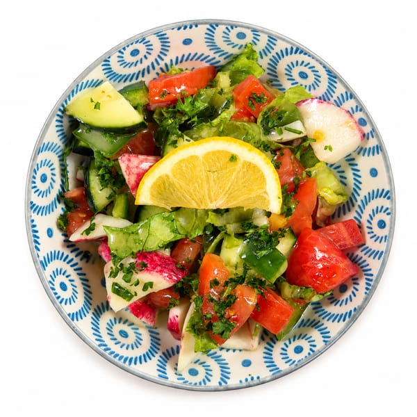 Fresh garden salad with lettuce, tomatoes, cucumbers, radishes, and a lemon slice in a patterned bowl.
