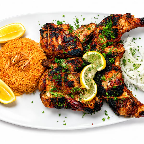 Grilled chicken with rice, lemon wedges, and sliced onions on a white platter.