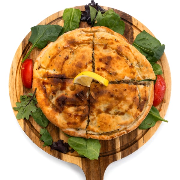 Golden-brown savory pastry, cut into quarters, drizzled with sauce, garnished with lemon, spinach, and tomatoes.